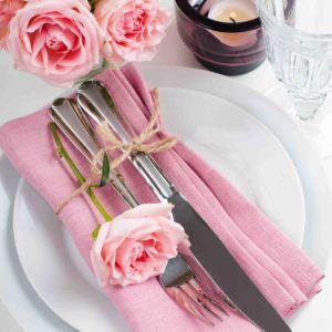 22621109 - beautiful festive table setting with roses, candles, shiny new cutlery and napkins on a white tablecloth.